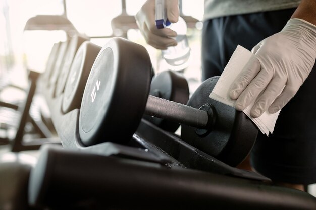 Primer plano de atleta desinfectando pesas de mano en un gimnasio