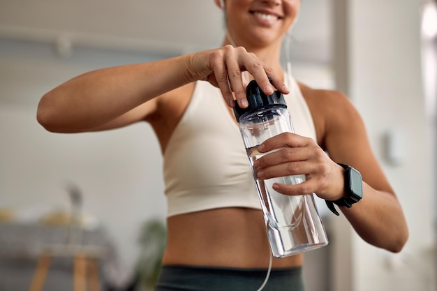 Primer plano de una atleta femenina sedienta que abre una botella de agua en casa