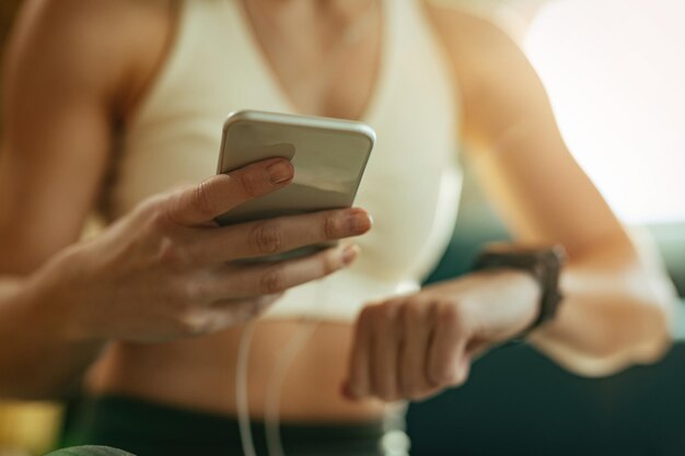 Primer plano de una atleta que usa un teléfono móvil mientras revisa la frecuencia cardíaca en el reloj de pulsera