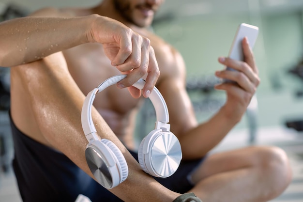 Primer plano de atleta sosteniendo auriculares mientras usa un teléfono inteligente en un gimnasio