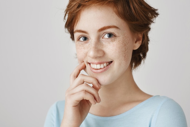 Primer plano de una atractiva chica pelirroja coqueta sonriendo y mirando adorable