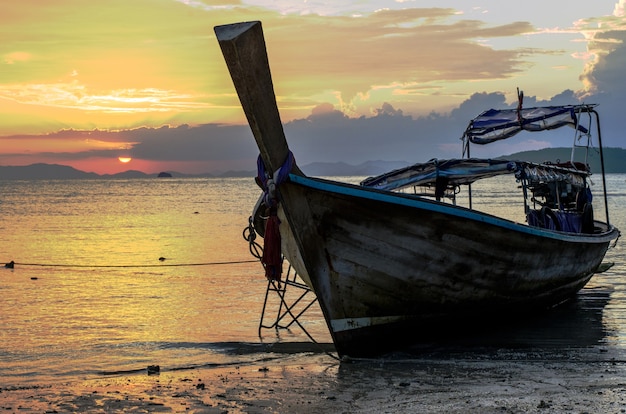 Primer plano de un barco de madera en la playa rodeada por el mar bajo un cielo nublado durante la puesta de sol