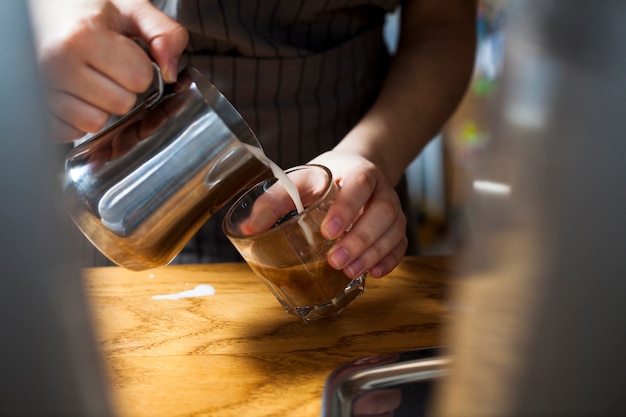 Primer plano de barista mano preparando café con leche sobre mesa de madera