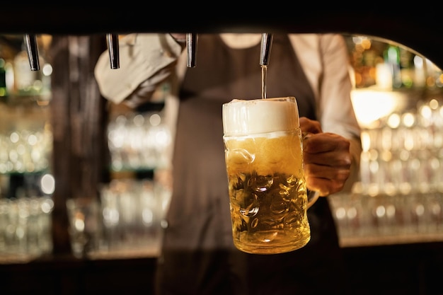 Primer plano de barista vertiendo cerveza del grifo de cerveza mientras trabaja en un pub.