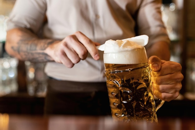 Primer plano de barman quitando espuma de cerveza mientras vierte cerveza en un pub