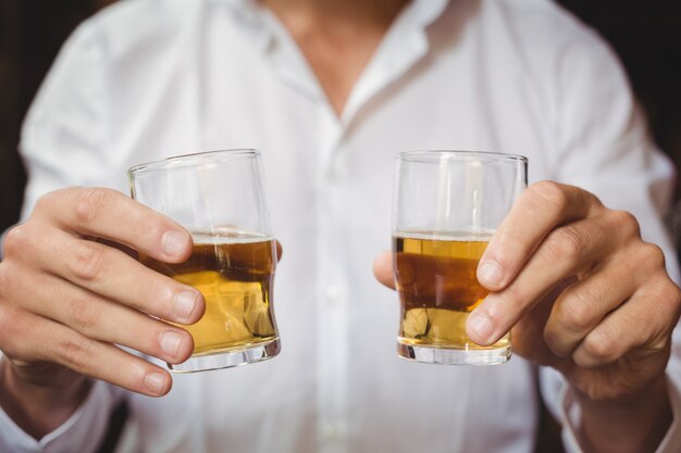 Primer plano de barman con vasos de chupito de whisky en barra de bar