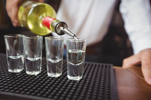 Primer plano de barman vertiendo tequila en vasos de chupito