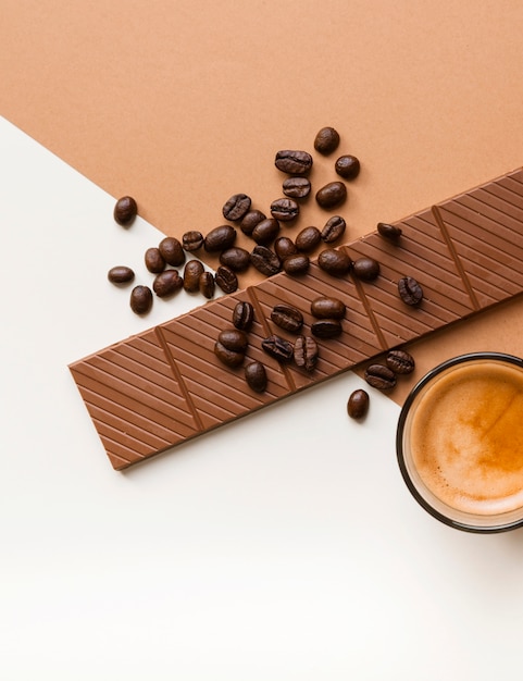 Primer plano de barra de chocolate y granos de café tostados con vaso de café sobre doble fondo