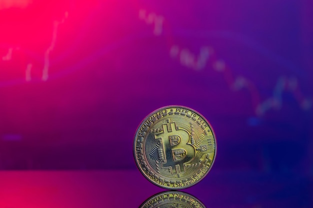 Primer plano de un Bitcoin dorado sobre una superficie reflectante rosa y azul y el histograma