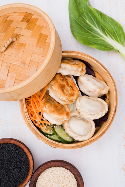 Primer plano de bolas de masa hervida cocidas al vapor chinas con la ensalada en cesta del vapor con las semillas de sésamo blancos y negros