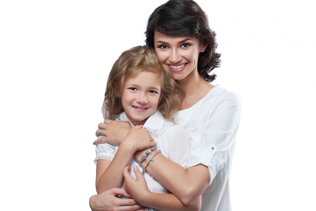 Primer plano de una bonita pareja familiar: hermosa madre y su pequeña hija agradable. Son muy felices con bonitas sonrisas. Llevan camisetas blancas. Se hizo la foto