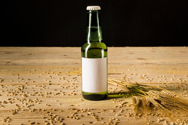 Primer plano de una botella alcohólica y espigas de trigo en un tablón de madera