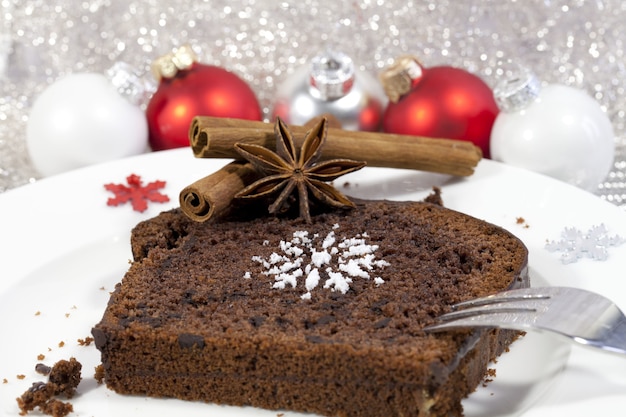 Foto gratuita primer plano de un brownie con canela y adornos de árbol de navidad rojo en el fondo