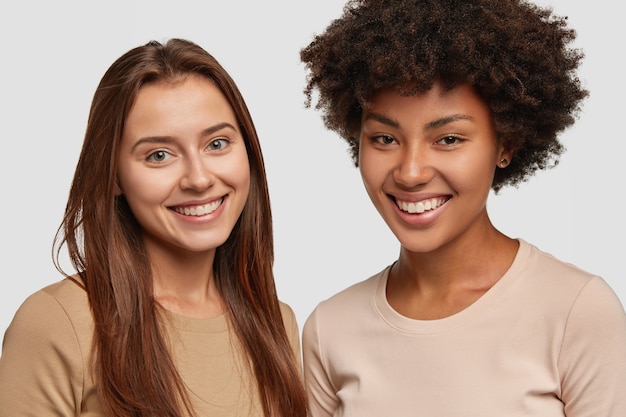 Primer plano de buenas dos mujeres positivas tienen tiernas sonrisas en los rostros