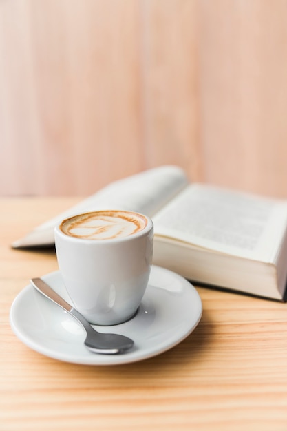 Primer plano de café con leche y libro abierto en la mesa de madera