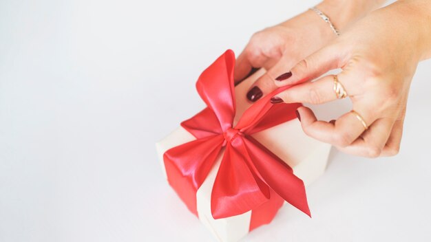 Primer plano de la caja de regalo de desenrollar de la mano de la mujer en el fondo blanco