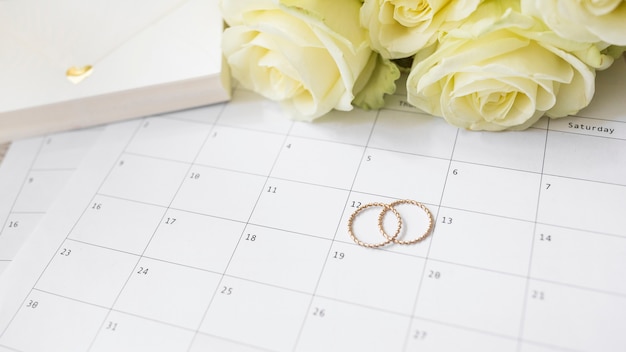 Primer plano de caja de regalo; Rosas y anillos de boda en el calendario.