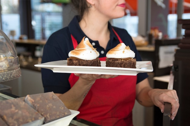 Primer plano de la camarera que sirve pastel de chocolate con crema batida