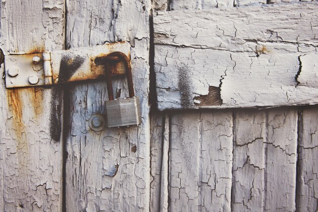 Primer plano de un candado viejo oxidado en una puerta blanca desgastada de madera