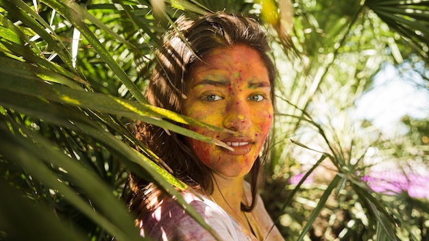 Primer plano de la cara de la mujer cubierta con polvo de color holi de pie cerca de las plantas