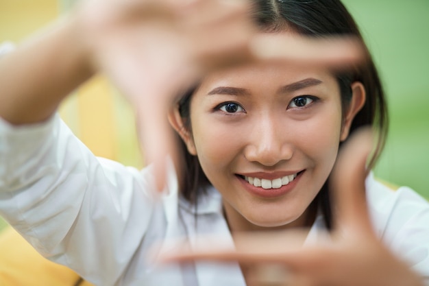 Primer plano de la cara sonriente que enmarca de la mujer con los dedos