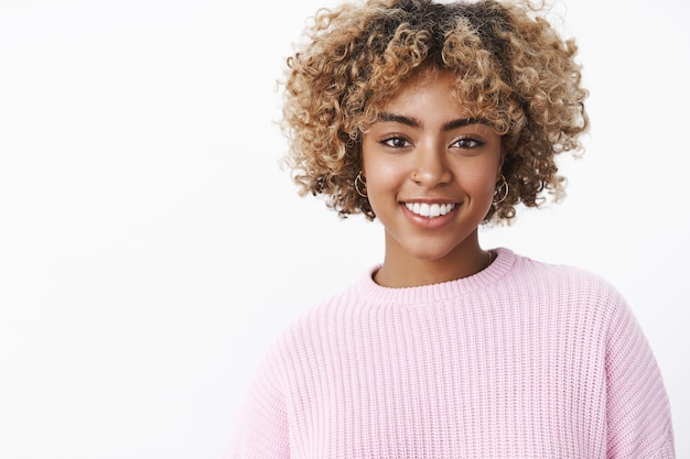 Primer plano de la carismática chica de piel oscura agradable de aspecto amistoso feliz con la nariz perforada, sonrisa perfecta de pie encantado y linda sobre la pared blanca en suéter disfrutando de la cena de vacaciones en familia