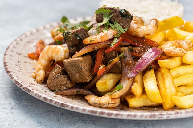 Primer plano de carne asada con salsa, verduras y patatas fritas en un plato sobre la mesa