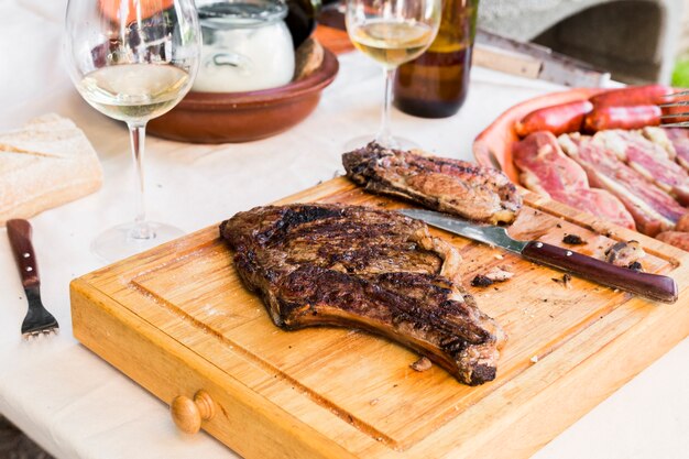 Primer plano de una carne cocida y un cuchillo en la tabla de cortar de madera