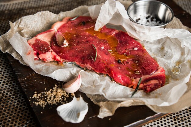 Primer plano de carne cruda con condimentos y hierbas sobre una tabla de madera