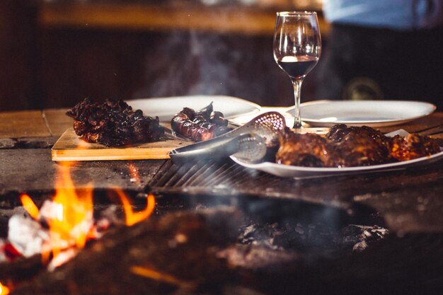 Primer plano de carne a la parrilla y una copa de vino cerca de la chimenea