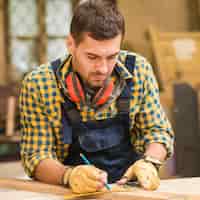 Foto gratuita primer plano de un carpintero masculino que mide el tablón de madera largo con la regla
