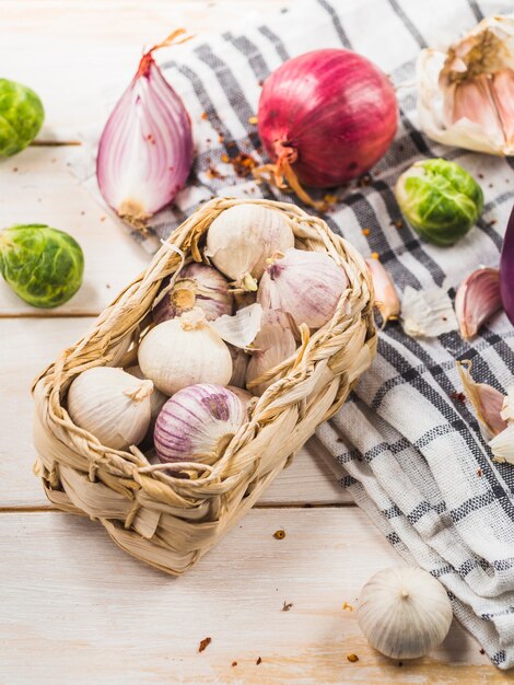 Primer plano de cebollas; coles de Bruselas; dientes de ajo y tela de patrón a cuadros en mesa de madera