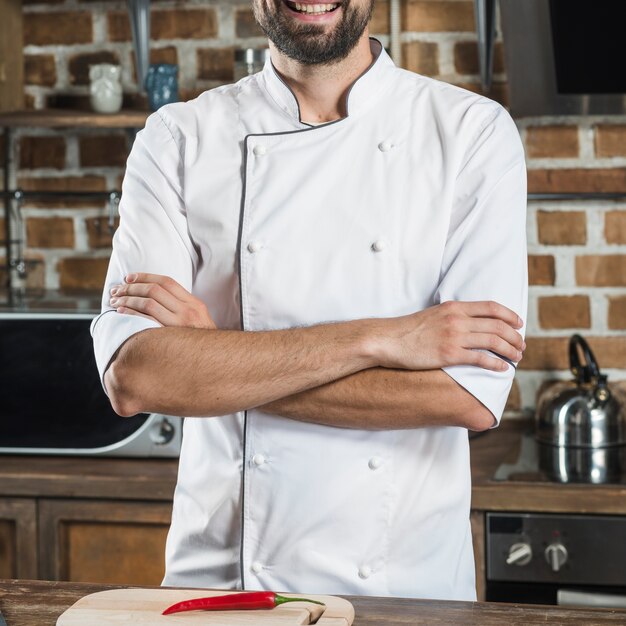 Primer plano del chef masculino con el brazo cruzado de pie detrás del mostrador de la cocina