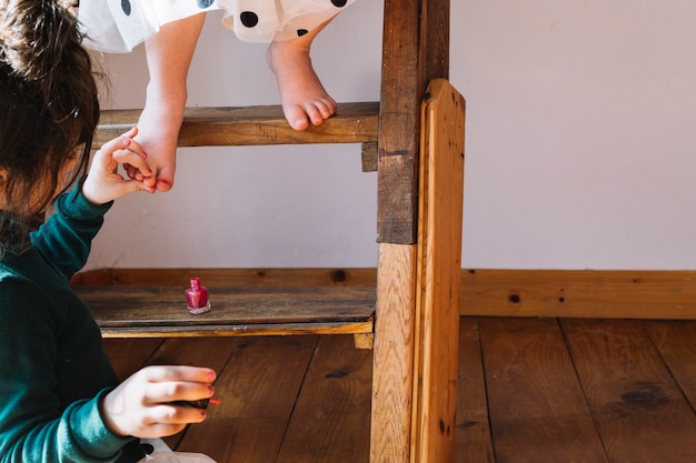 Primer plano de una chica aplicando esmalte de uñas en la uña de su hermana en casa