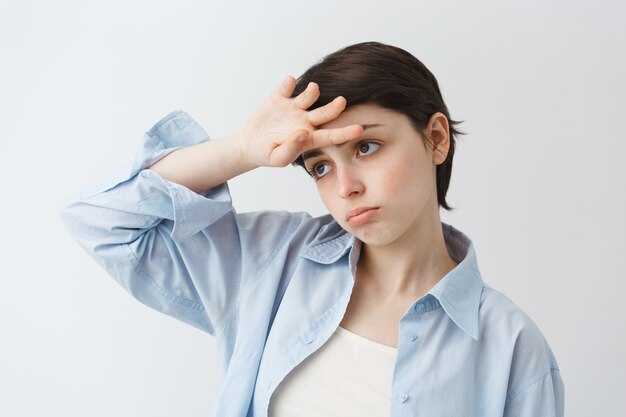 Primer plano de chica atractiva cansada y triste tomboy tomados de la mano sobre la frente, actuando dramáticamente