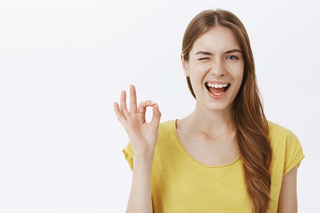 Primer plano de una chica atractiva y descarada sonriendo y guiñando un ojo, muestra un gesto de aprobación