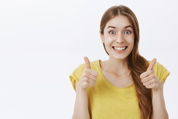 Primer plano de una chica atractiva sonriendo y mostrando el pulgar hacia arriba en señal de aprobación, de acuerdo o como algo