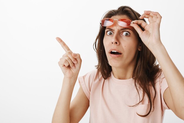 Primer plano de chica divertida con gafas de sol posando contra la pared blanca