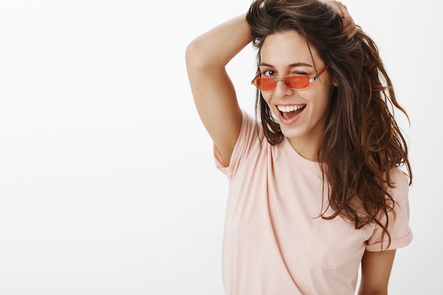 Foto gratuita primer plano de chica elegante con gafas de sol posando contra la pared blanca