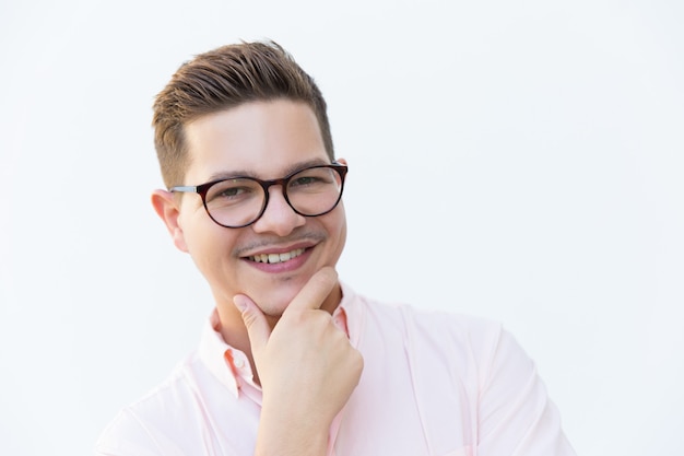 Primer plano de un chico alegre en gafas tocando la barbilla