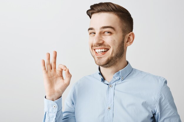 Primer plano de un chico feliz seguro que muestra un gesto bien, no hay problema, todo está bien, alaba el buen trabajo, dice bien hecho