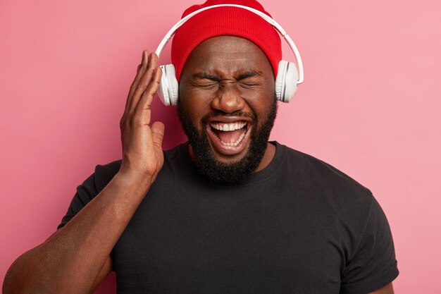 Primer plano de un chico de piel oscura feliz emocional disfruta de escuchar música con alto volumen en auriculares