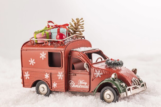 Primer plano de un coche de juguete con adornos navideños sobre nieve artificial sobre un fondo blanco.