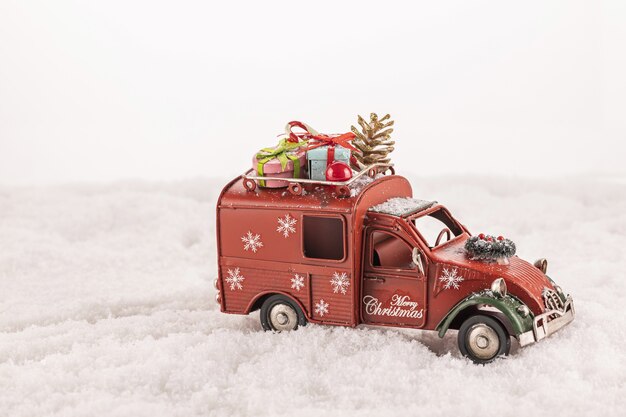 Primer plano de un coche de juguete con adornos navideños sobre nieve artificial sobre un fondo blanco.
