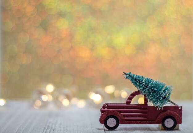 Primer plano de un coche de juguete con un árbol de Navidad con luces borrosas en el fondo