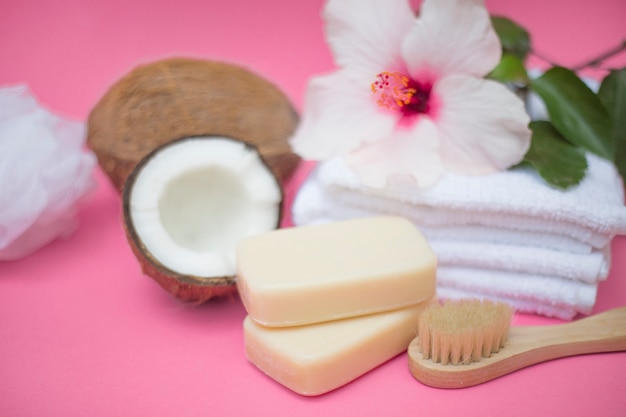 Primer plano de coco; jabón; cepillo; flores y toallas sobre fondo rosa