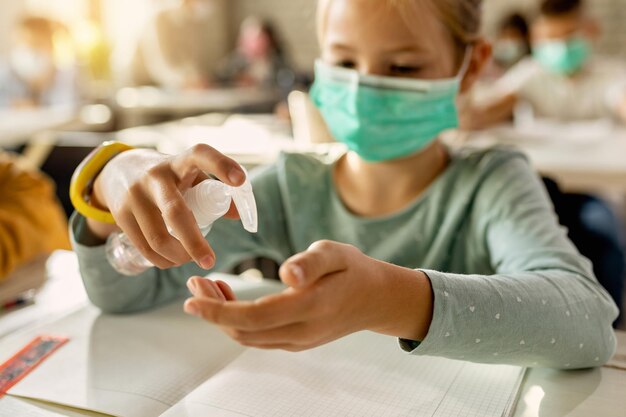 Primer plano de una colegiala usando desinfectante para manos en el aula