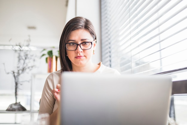 Foto gratuita primer plano de la computadora portátil en frente de una mujer joven con gafas