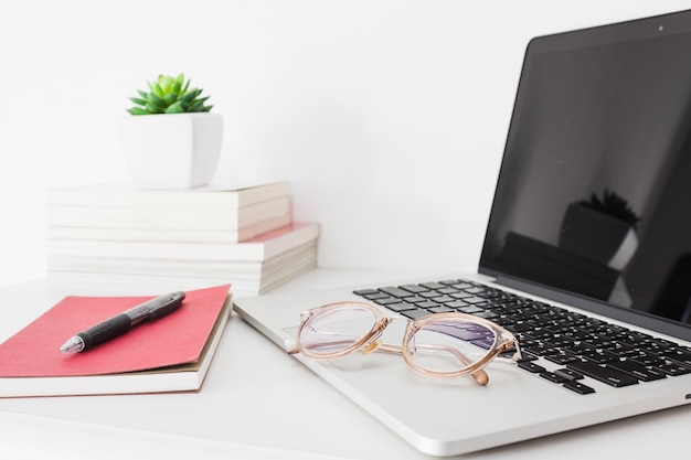 Primer plano de la computadora portátil; gafas; pluma y diario en el escritorio