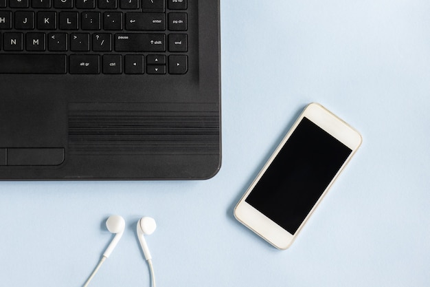 Primer plano de una computadora portátil, teléfono inteligente y auriculares sobre una superficie azul claro